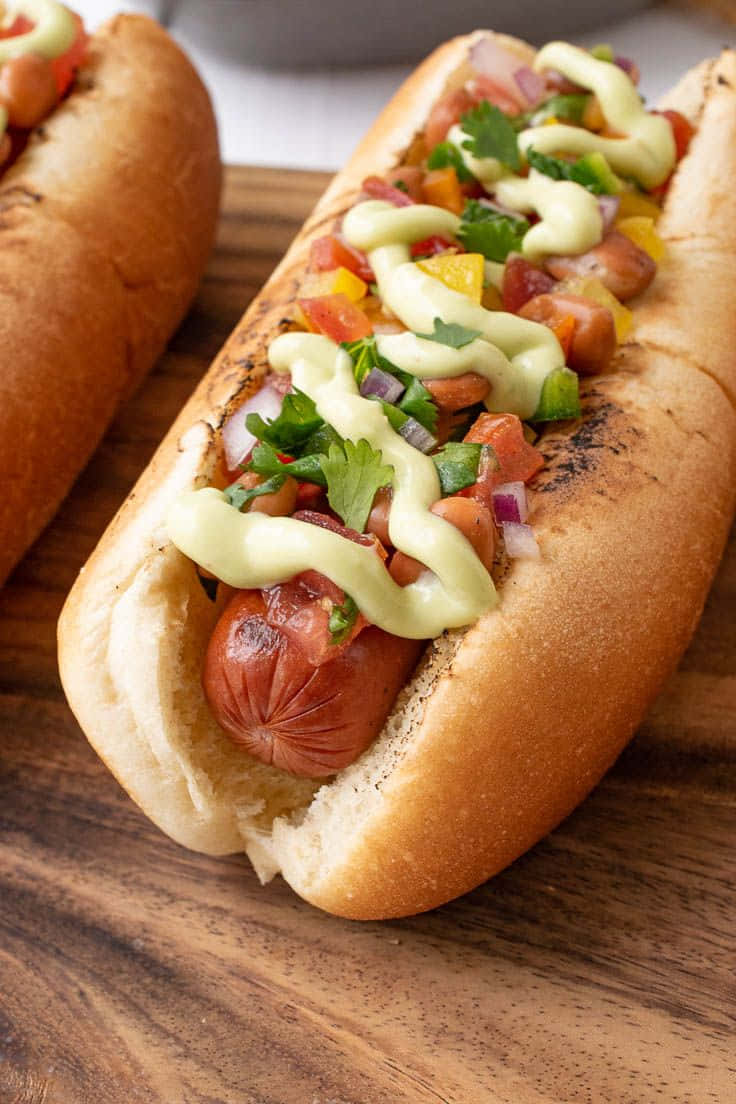 doi hot dog-uri cu toppinguri pe o placă de tăiat din lemn Fundal