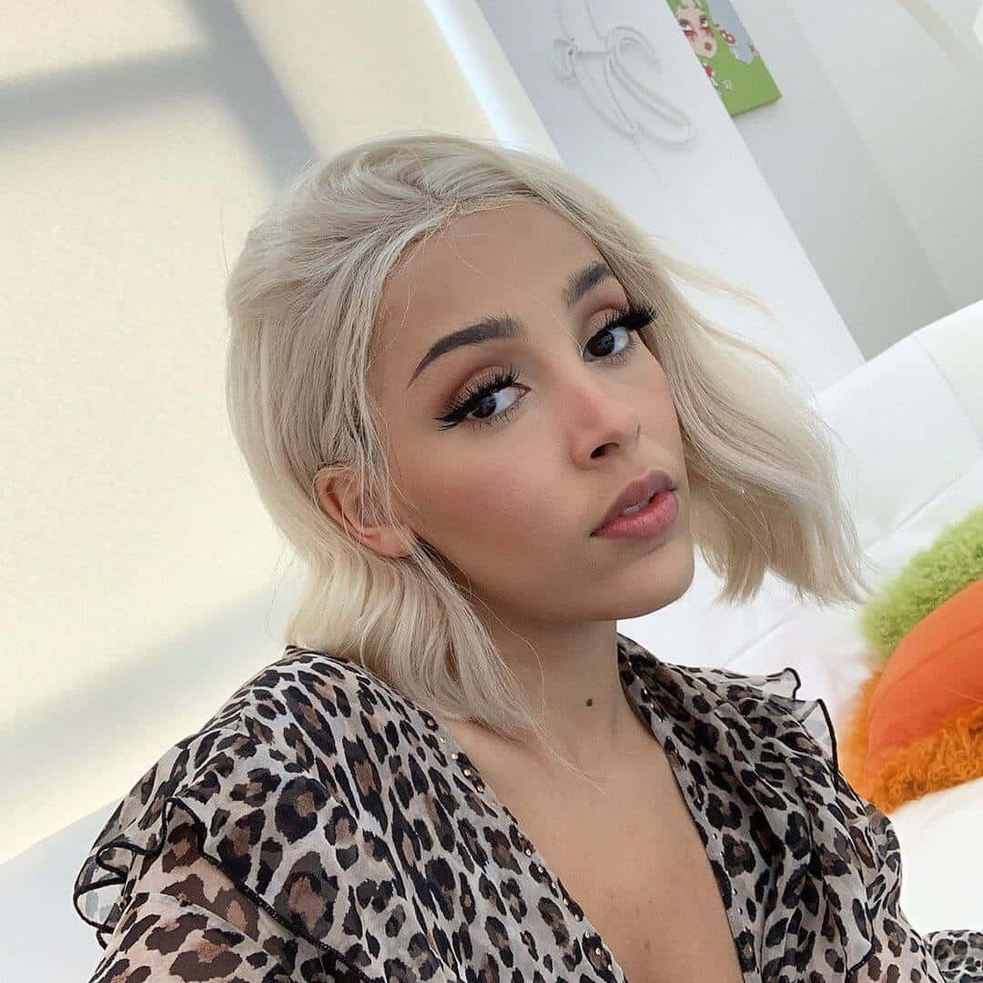Doja Cat își etalează frumusețea cu fard de pleoape sclipicios și un zâmbet strălucitor. Fundal