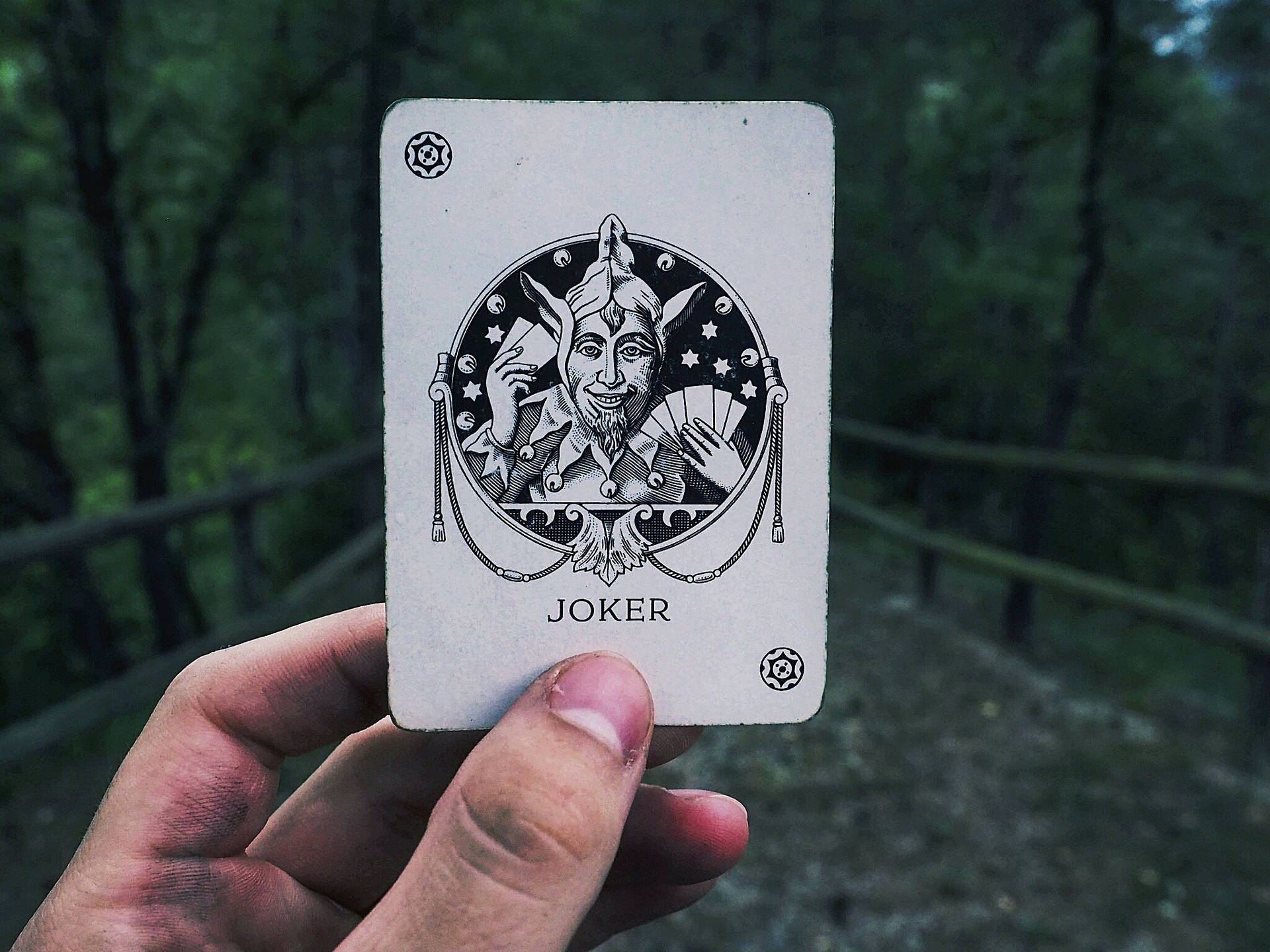 Mână ținând o carte joker pe un fundal neclar de drum de țară. — Joker Fundal