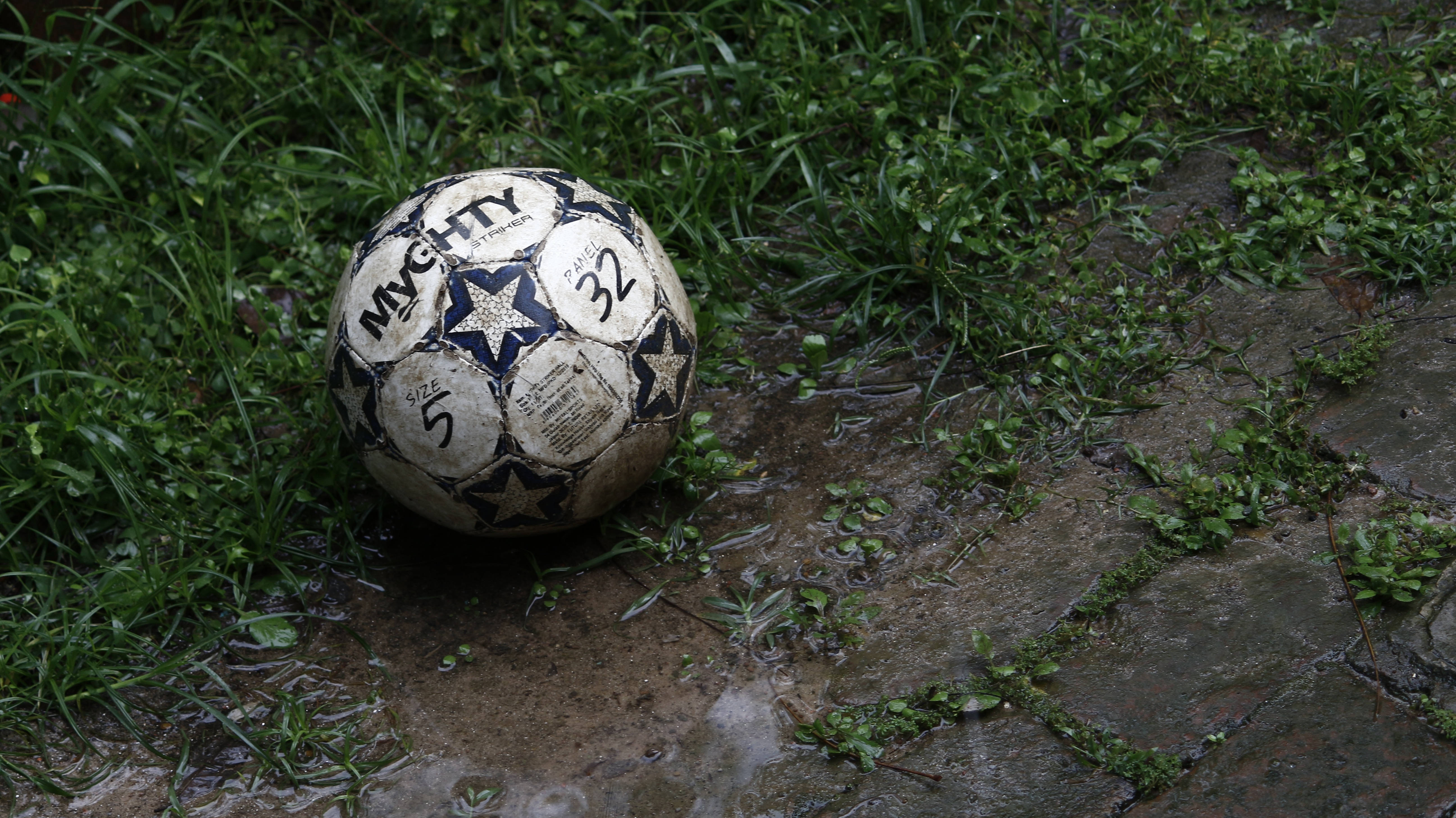 O minge de fotbal noroioasă zace necolectată în iarbă. Fundal