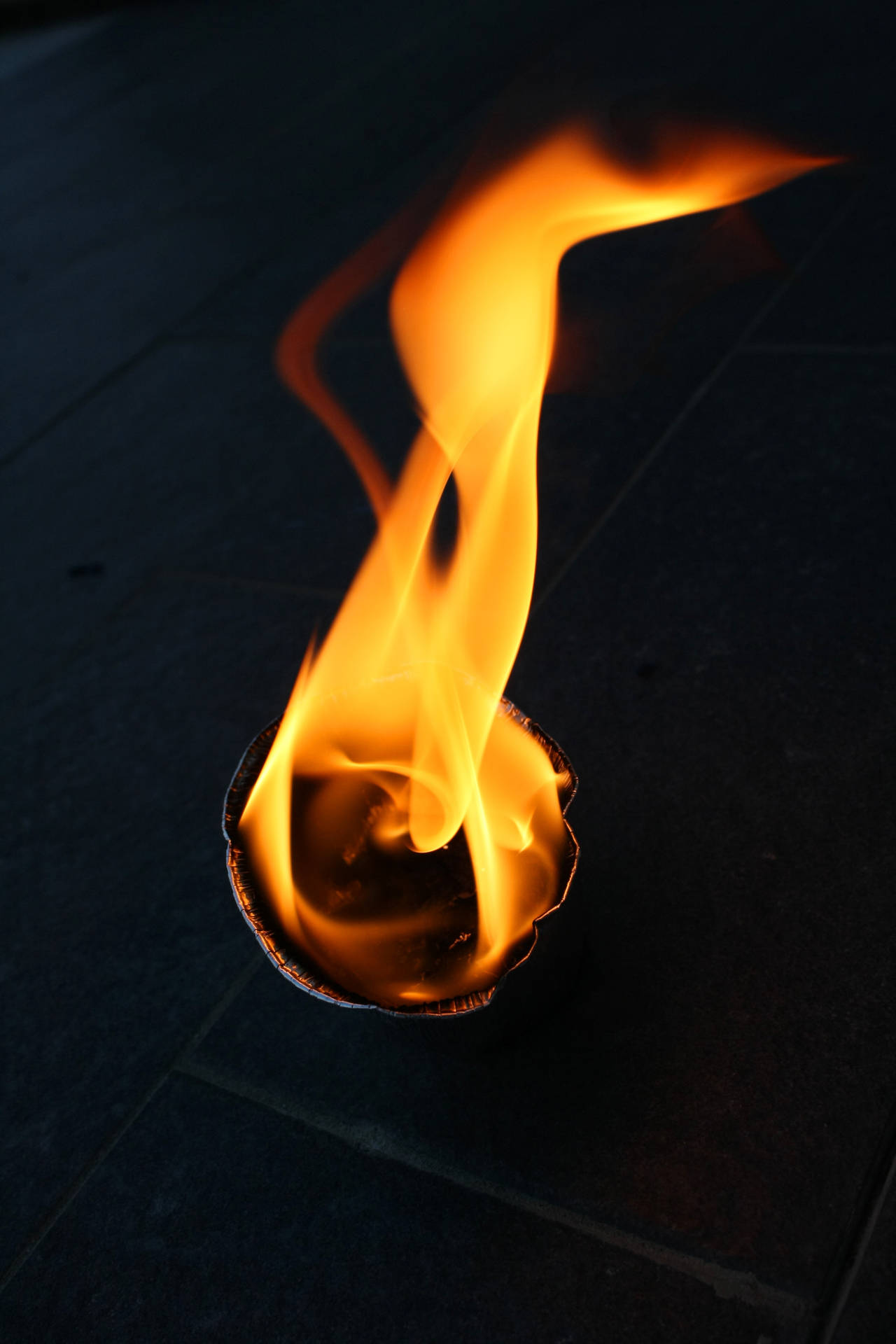 Bucată rotundă de hârtie arzând pe podea. Prim-plan al flăcării. Obiect care arde într-o cameră întunecată.
