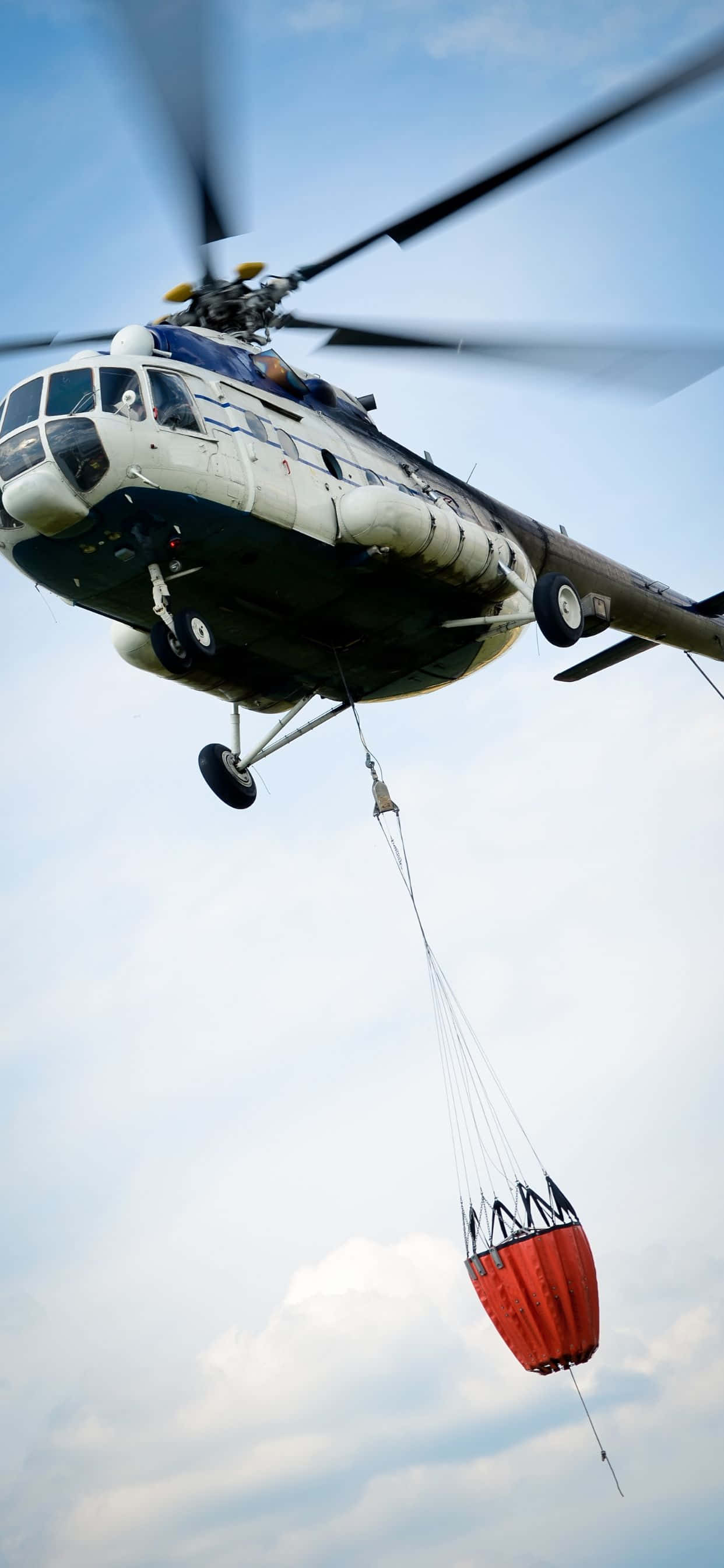 un elicopter zboară cu o geantă roșie atașată de el Fundal