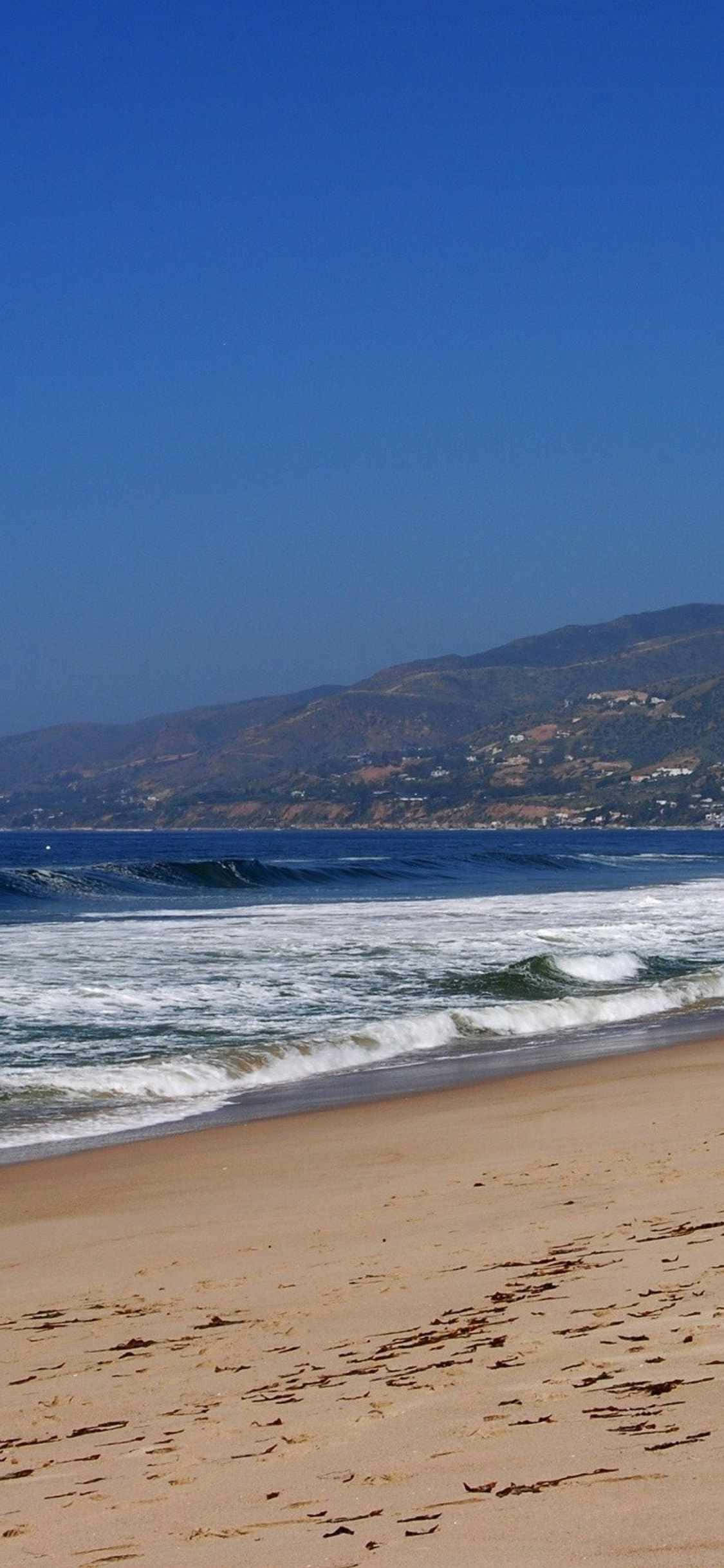 un om merge pe plajă cu o placă de surf Fundal