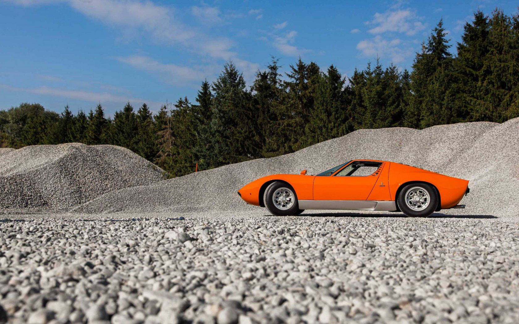 Un rafinat Lamborghini Miura portocaliu pe un drum de pietriș. Fundal