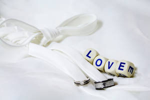 Cuvântul „Love” scris pe patru zaruri albe, lângă două verighete argintii și negre legate cu o panglică albă, așezate pe o foaie albă.