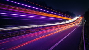O expunere lungă a unei autostrăzi cu benzi neon și urme de lumini de mașini.