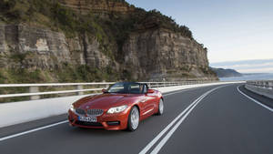 Tapet cu BMW Z4 portocaliu pe drum lângă munte