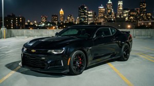 Un Camaro ZL1 negru parcat pe un acoperiș al unei parcări, cu orizontul orașului noaptea.