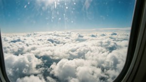 Vedere aeriană din avion cu cer albastru deasupra și nori albi dedesubt.