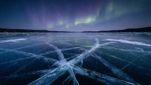 Suprafața unui lac înghețat reflectând aurora boreală pe un cer întunecat de iarnă.