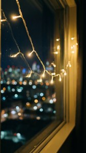 Lumini de basm lângă o fereastră, cu bokeh urban nocturn. — Estetic de Crăciun Fundal