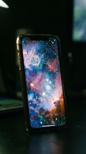 Ecranul iPhone 17 stralucește cu un wallpaper galaxie în întuneric. — iPhone 17 Fundal