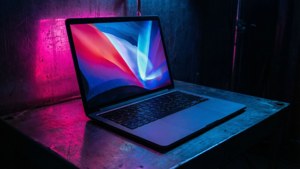 Un MacBook inspirat de cyberpunk, cu reflexii neon într-o cameră întunecată.