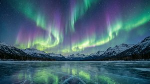 Aurora boreală peste un lac înghețat cu munți acoperiți de zăpadă.