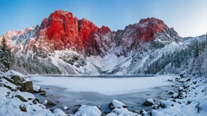 Peisaj de iarnă cu un munte roșu acoperit de zăpadă și un lac înghețat