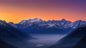 Vedere ultra-largă impresionantă a munților acoperiți de zăpadă la răsărit, cu vale cețoasă.