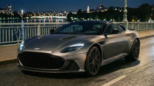 Aston Martin DBS Superleggera pe un pod noaptea, cu lumini ale orașului. imagine de fundal