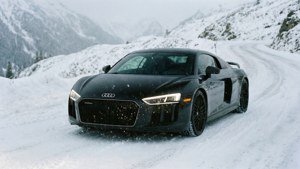 Un Audi R8 negru circulă pe un drum alpin înzăpezit, cu fulgi de nea căzând. imagine de fundal