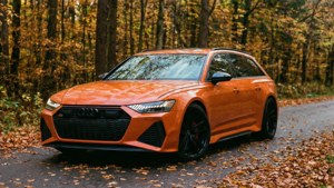 Un Audi RS6 Avant portocaliu pe un drum de pădure toamna, cu frunze care cad.