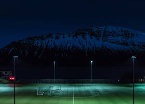Teren de fotbal noaptea, iluminat de stâlpi de lumină, fundal.